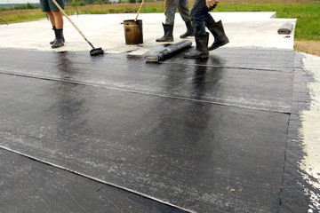 Roofer worker painting bitumen praimer at concrete surface by the roller brush Waterproofing