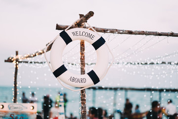Life bouy with welcome aboard text on it hanging on wooden pole with beautiful bokeh background.