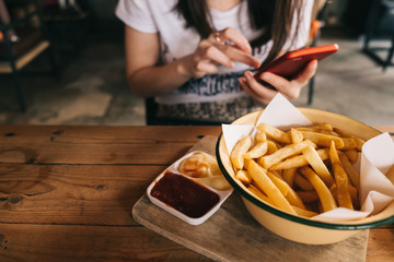 Woman eating french fries while using smart phone.