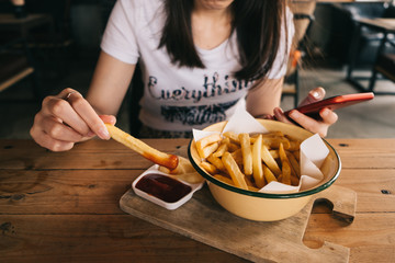 Woman eating french fries while using smart phone.