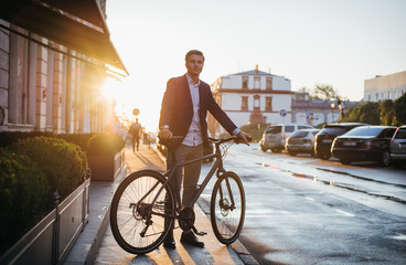 Handsome young man with his bicycle on the street in city center during sunrise