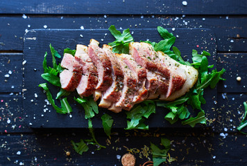Homemade sliced roasted duck fillet with spices and arugula on dark wooden board top view (series...