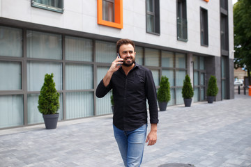 Fototapeta premium A man with a beard goes and speaks by phone