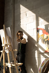 Portrait of handsome male artist painting picture on easel with inspiration in art studio lit by sunlight, copy space