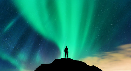 Aurora and silhouette of alone standing man on the mountain peak. Lofoten islands, Norway. Aurora...