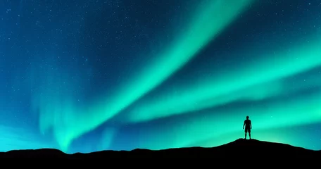 Poster Aurora en silhouet van alleenstaande man op de heuvel. Lofoten eilanden, Noorwegen. Aurora borealis en jonge man. Hemel met sterren en groene poollichten. Nachtlandschap met noorderlicht. Concept © den-belitsky