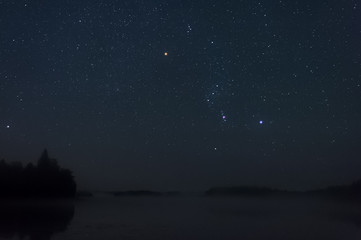 Orion constellation above misty lake.