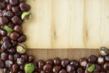 Creative autumn decoration with copy space - frame from chestnuts arranged on wood planks.