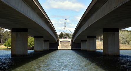 Commonwealth Bridge over Lake Burley Griffin in Australia capital city Canberra. Australian Parliament House at the end of the bridge. Bridges two road route structures over lake waters.