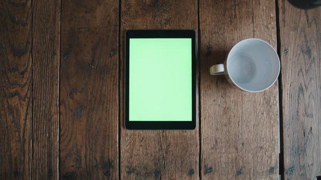 Filling coffee mug next to tablet on wood table