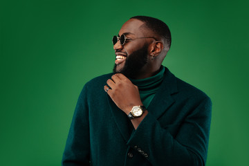 Man portrait. Style. Handsome Afro American guy in green jacket and sun glasses is smiling, on a green background