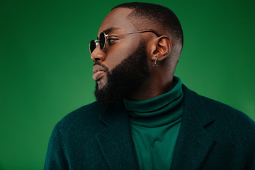 Man portrait. Style. Handsome Afro American guy in green jacket is looking away, on a green background