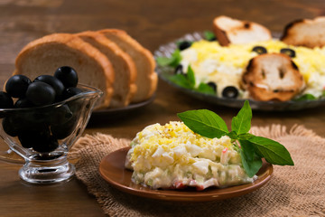 A portion of a cold snack on a round plate, pickled olives, green basil  leaves.