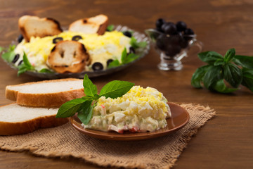 A portion of cold appetizer of eggs, cheese, crab meat with mayonnaise and green basil  leaves, pickled olives, wooden background.
