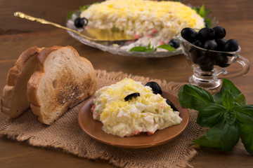 A portion of egg salad with crab meat and cheese, toasted toast, green basil  leaves, marinated black olives.
