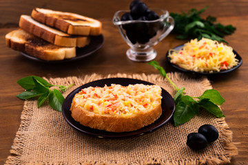 Breakfast of toasted toast with crab meat and melted grated cheese, green basil  leaves, marinated black olives.