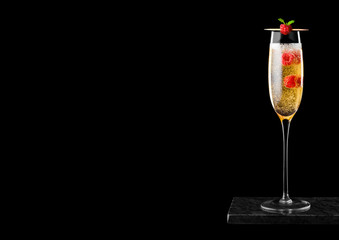 Elegant glass of yellow champagne with raspberries and bubbles inside black marble board on black background.Space for text
