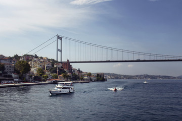 View of a white yacht, small boats, FSM bridge, Bosphorus and European side of Istanbul. It is a sunny summer day.