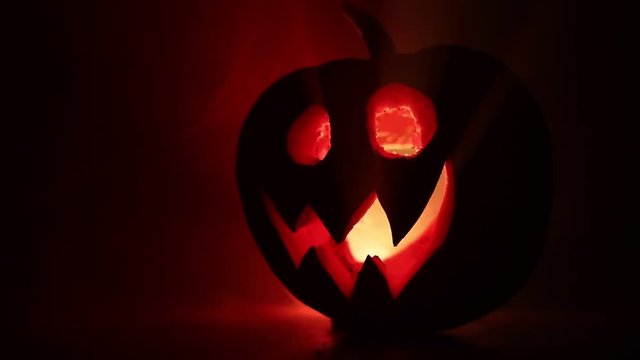 Halloween pumpkin smile and scrary eyes for party night. Close up view of scary Halloween pumpkin with eyes glowing inside at black background. Selective focus