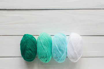 knitting clew in row on white wooden background, pastel green and white colors, top view flat lay...