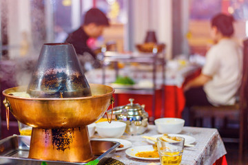 Chinese hot pot on the table with people eating on the background. Toned