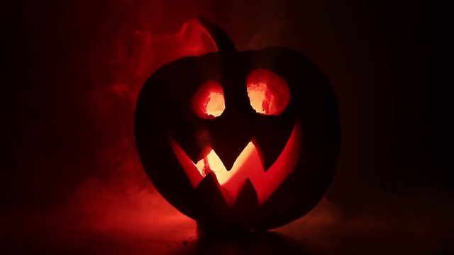 Halloween pumpkin smile and scrary eyes for party night. Close up view of scary Halloween pumpkin with eyes glowing inside at black background. Selective focus