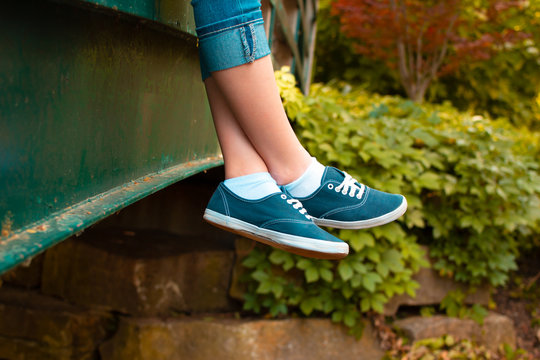 Girl sits dangling and crossed her legs on a green bridge in the park