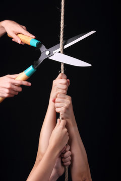 Group of people hanging from a rope and another person cutting the rope with big scissors. Concept for cutting off aid, or getting rid of competitors