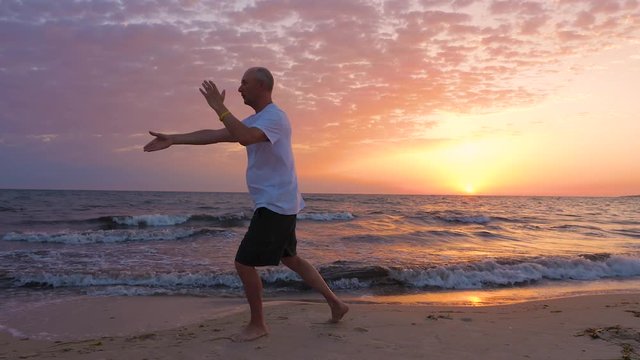 Sportive man practicing Tai Chi on seashore at sunrise