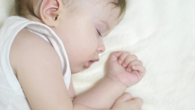 Small baby sleeps in his crib on white blanket. closeup