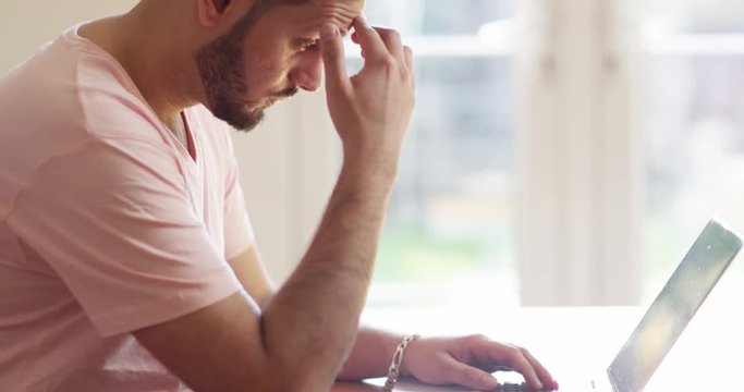 4K Tired & serious Asian man deep in thought while typing on laptop. Slow motion.