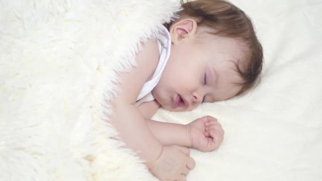 small child is sleeping in his crib covered with white blanket. closeup