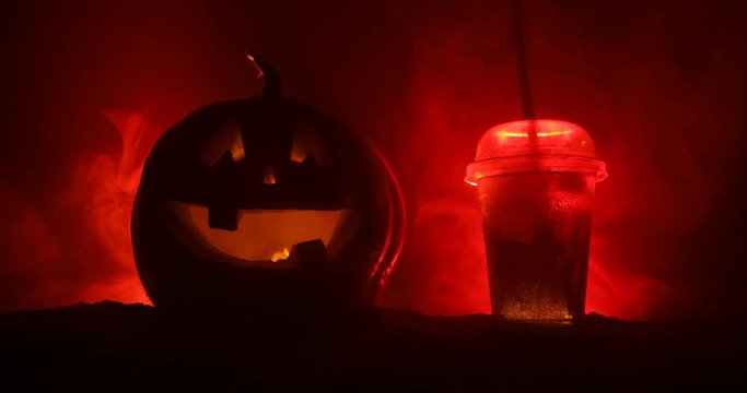 Halloween pumpkin orange cocktails. Festive drink. Halloween party. Funny Pumpkin with a glowing cocktail glass on a dark toned foggy background. Selective focus