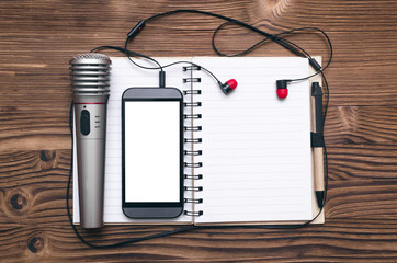 Mobile phone, blank page note pad, microphone and headphones on the table. Audio recording studio...