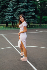Fototapeta premium Charming brunette female dressed in a pink dress posing on the basketball court.