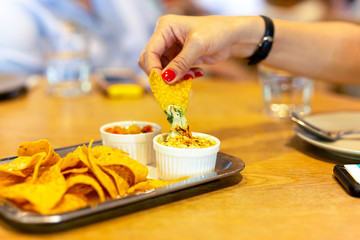 Womans hand with red color nail having a tortilla chip with nacho cheese sauce at lunch time.