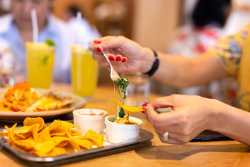 Womans hand with red color nail having a tortilla chip with spinach nacho cheese sauce with friend.