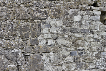 Close up view of a gray medieval castle stone wall with discoloration from lichens and moss