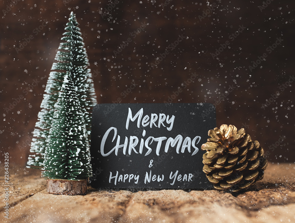 Aufkleber merry christmas and happy new year on blackboard with xmas tree and gold pine cone and snow falling 