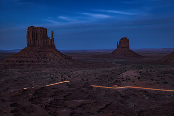 Long exposure of a car driving by the Mittens of Monument Valley at twilight