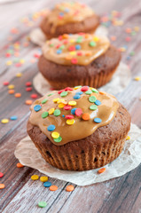 Chocolate muffins. With caramel and multi-colored tapping. Geometry. A wooden background is blurred.
