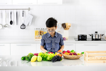 Young Asian boy looking to pile of fake fruits and vegetables in white clean modern kitchen