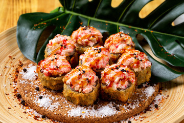 Closeup set of hot fried rolls with lava maki topping at wooden board background.
