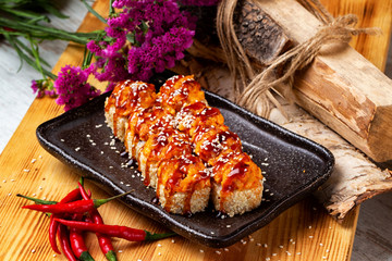 Set of hot sushi rolls with sesame, lava maki and teriyaki at decorated with flowers and chilli pepper wooden table background.