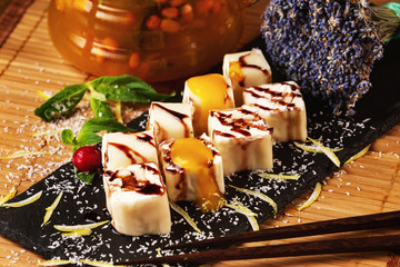Set of sweet japanese sushi rolls served with mango sauce decorated with teapot and flowers at restaurant table background.