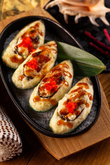 Verical top view image of mussels with cheese filling decorated with tobico and teriyaki at restaurant table background.