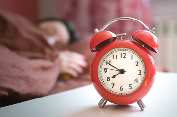Sleepy woman in the bed and a red alarm clock with eight o clock on the table at morning time.