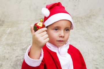 sad boy with santa claus costume holding christmas ball