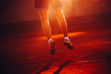 Fit sporty man on field, legs view, jumping at sunset