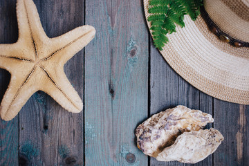 a hat, a fern leaf, a starfish, sea shells on the wooden background